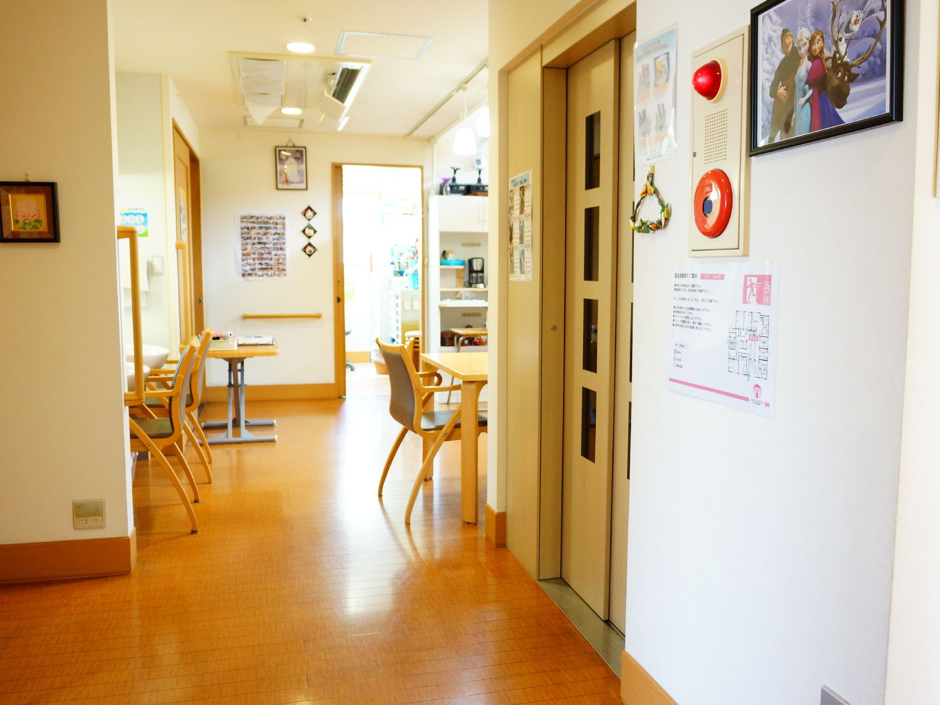 バリアフリーの仕切りのない広い食堂。テーブルとアーム付きの椅子が数脚置いてある。壁には適宜手すりが設置してある。