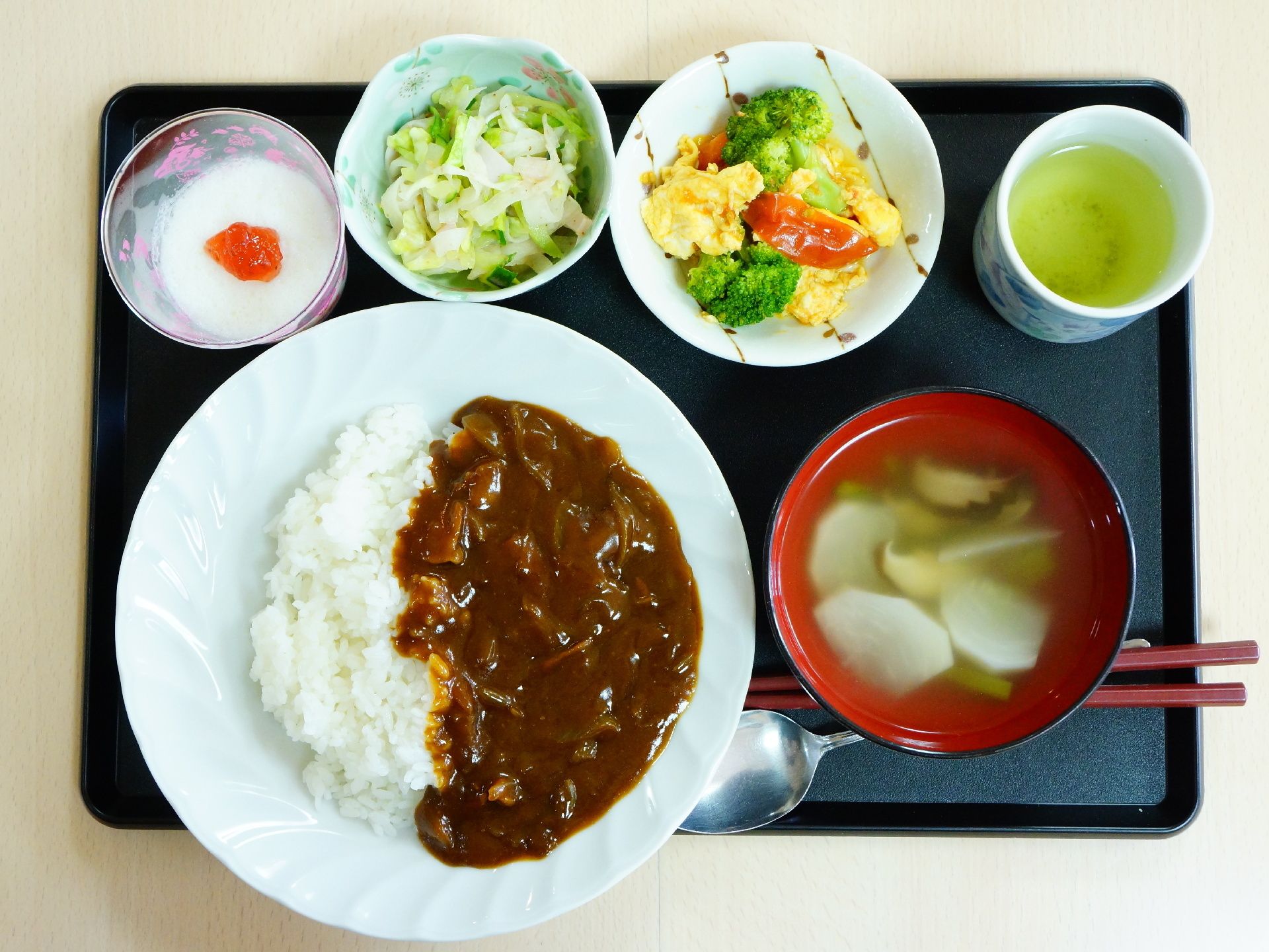 カレーライスをメインに、卵、ブロッコリー、トマトの炒め物、野菜の和え物、スープ、デザートなど彩豊かなメニュが並んでいる。