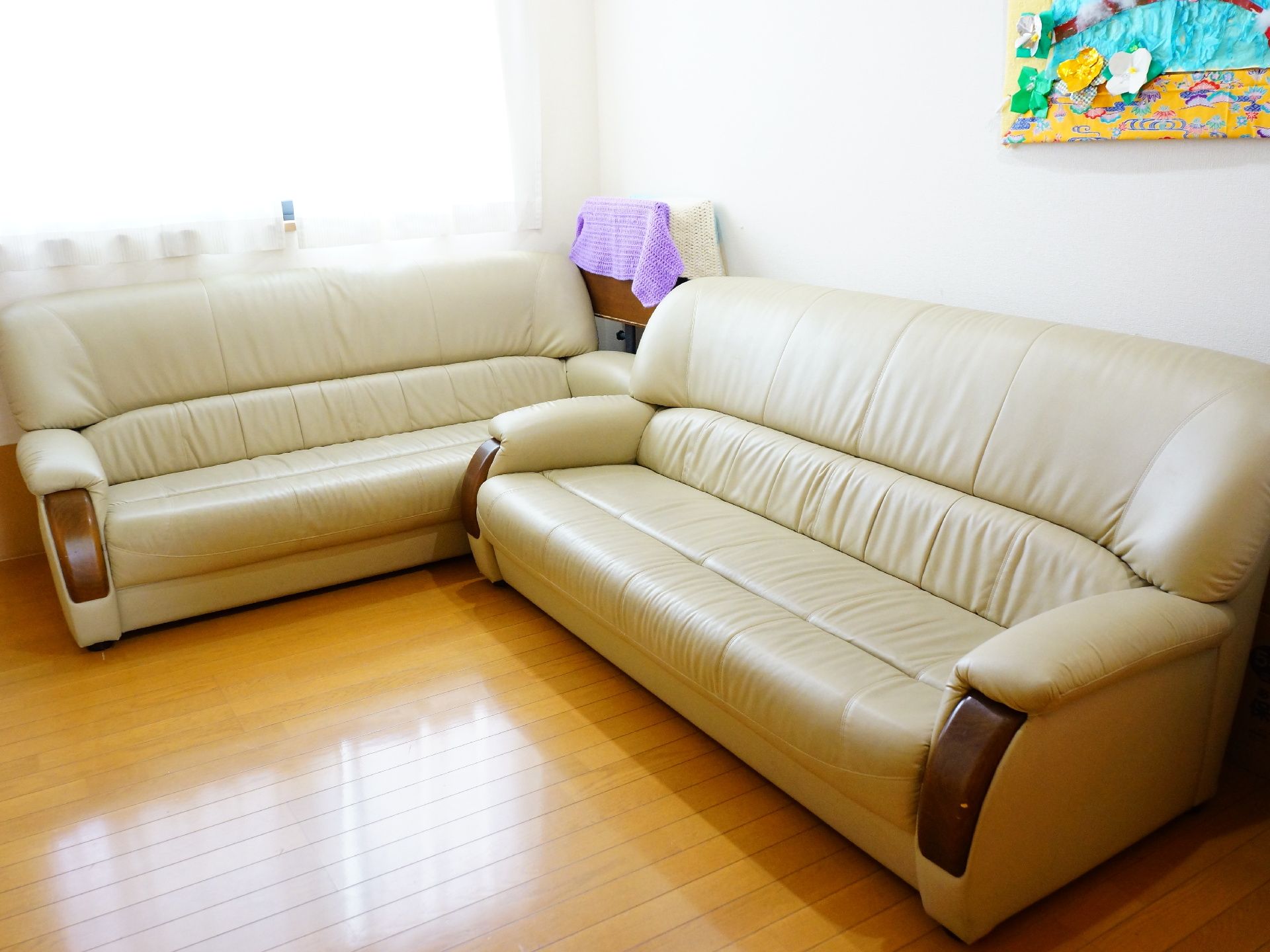 部屋にはベージュ色のソファーが2つ置かれている。ソファーはL字型の配置である。ソファーの後ろの壁には折り紙などで作られた作品がある。