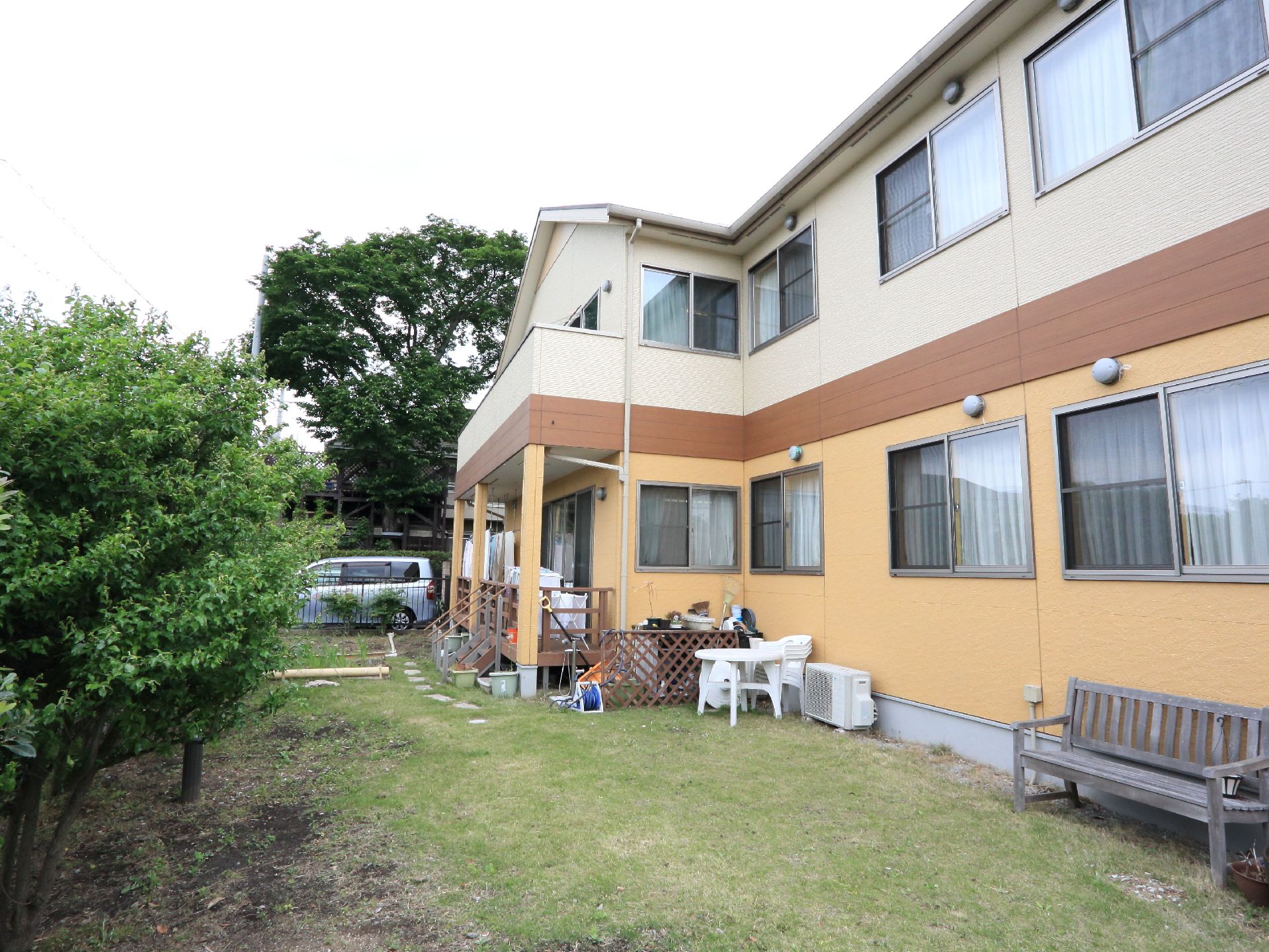 1階と2階で外壁の色が異なる施設建物には庭が併設されている。芝生が植えられている。木のベンチや白色のテーブル・椅子も置かれている。