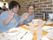 スープが置かれたレストランの壁際のテーブルで、入居者様とスタッフの２人が笑顔でピースをしながら写真に収まっている。