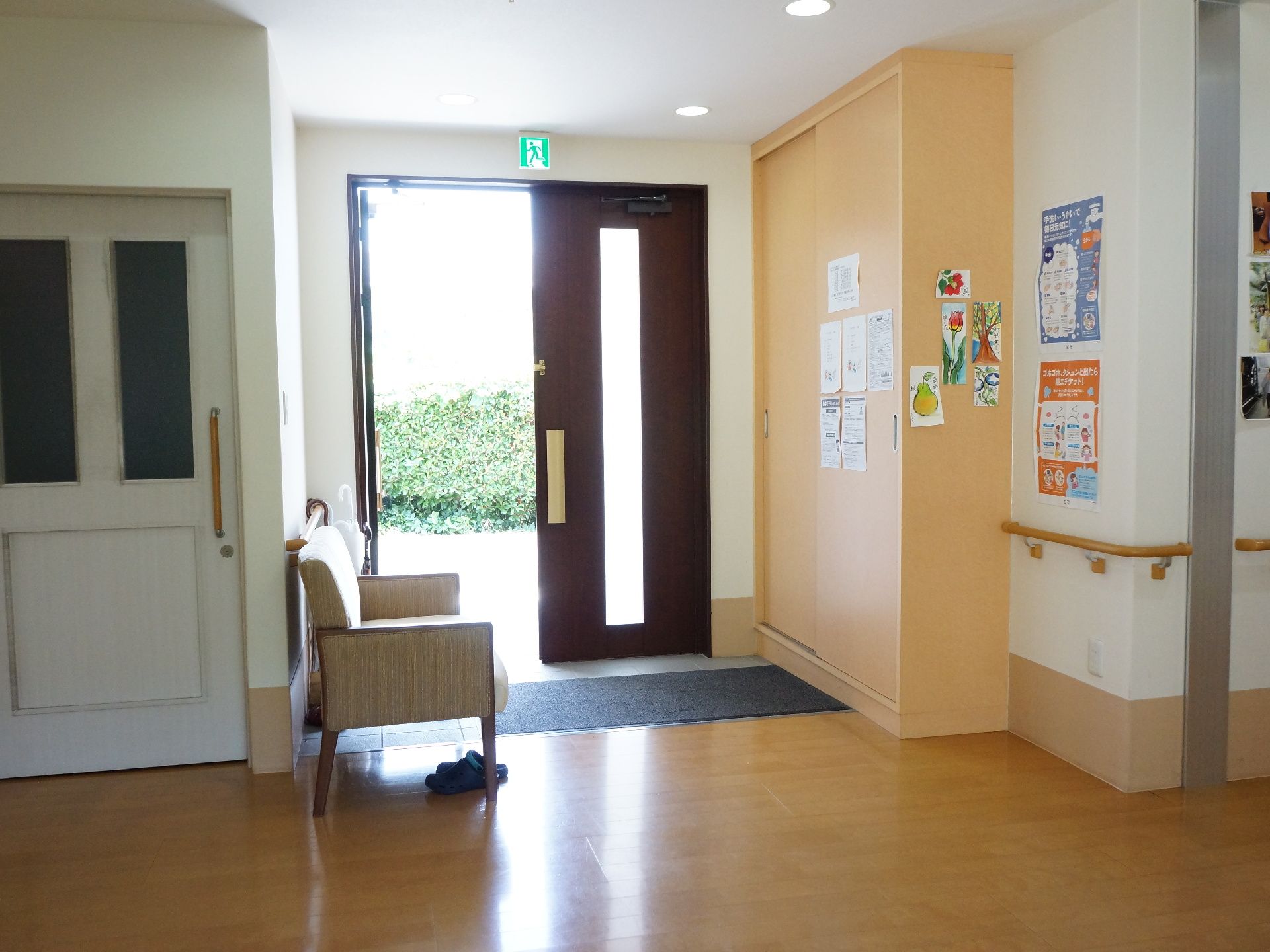 大きな段差がないエントランス。壁には手すりがあり、靴の脱ぎ履き用の椅子も7完備。周りの壁には入居者の作品も展示されている。