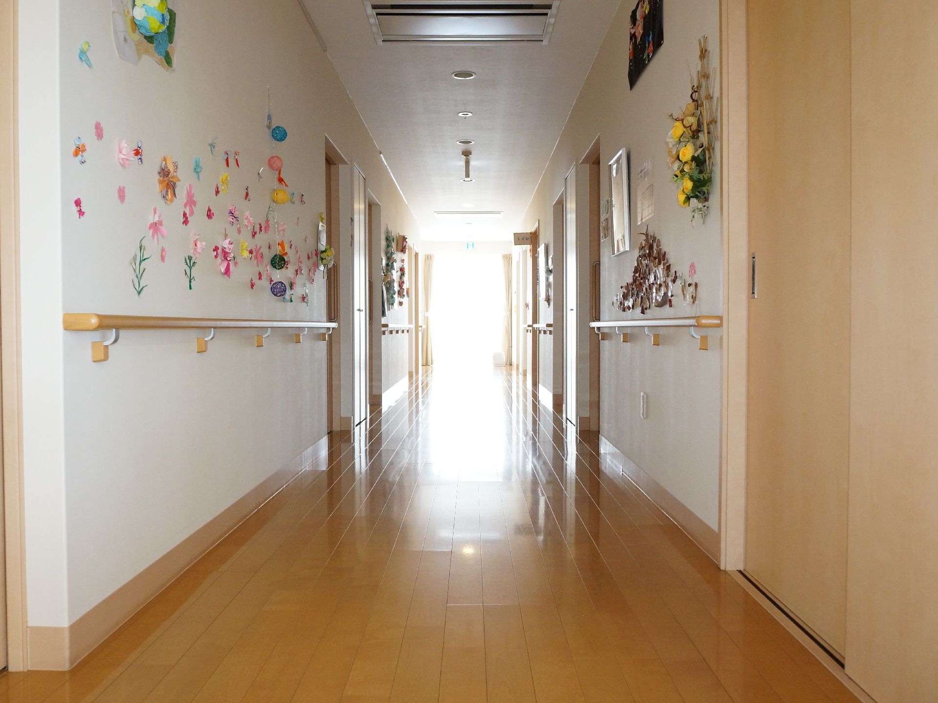 個室の扉は出入りしやすい引き戸タイプ。埋込式の空調が廊下の天井に設置してある。突き当りには窓があり日差しが差し込む。