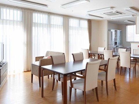 明るく広い室内には、４人用テーブルと肘付きの白いダイニングチェアが置かれている。テレビや冷蔵庫、食器棚もあって、アットホームな空間である。