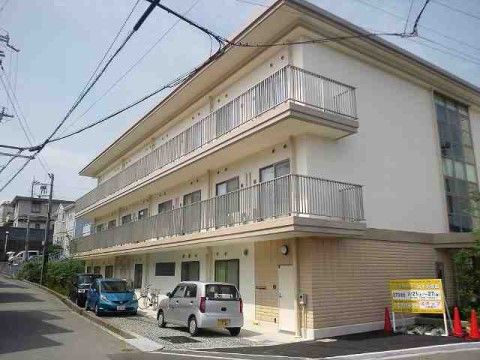 道路に沿って建てられているクリーム色の壁の3階建ての施設建物