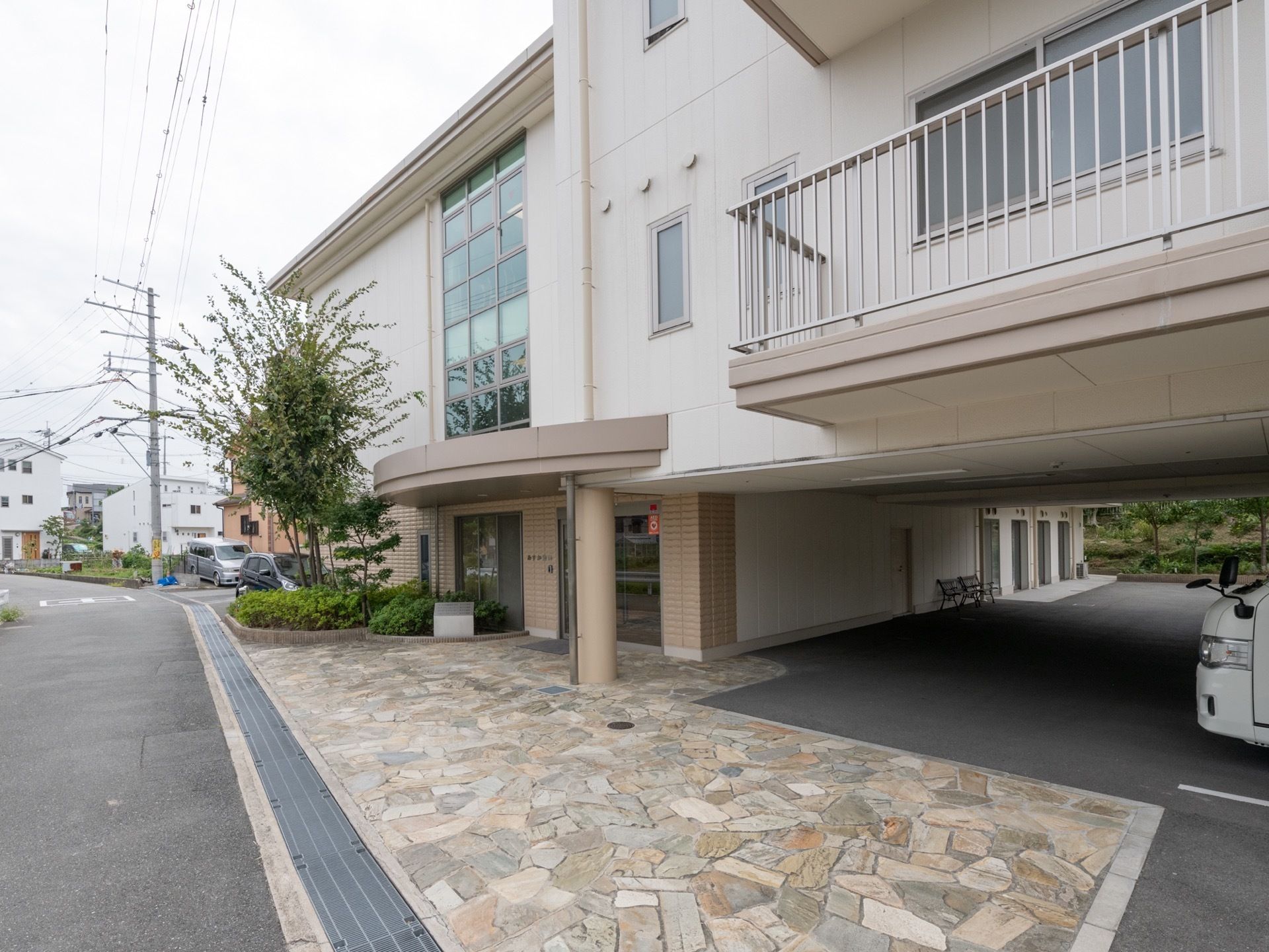 住宅街の道路に面した場所に施設がある。道路から入口までは段差がないよう整備されている。１階部分の半分は駐車場になっている。