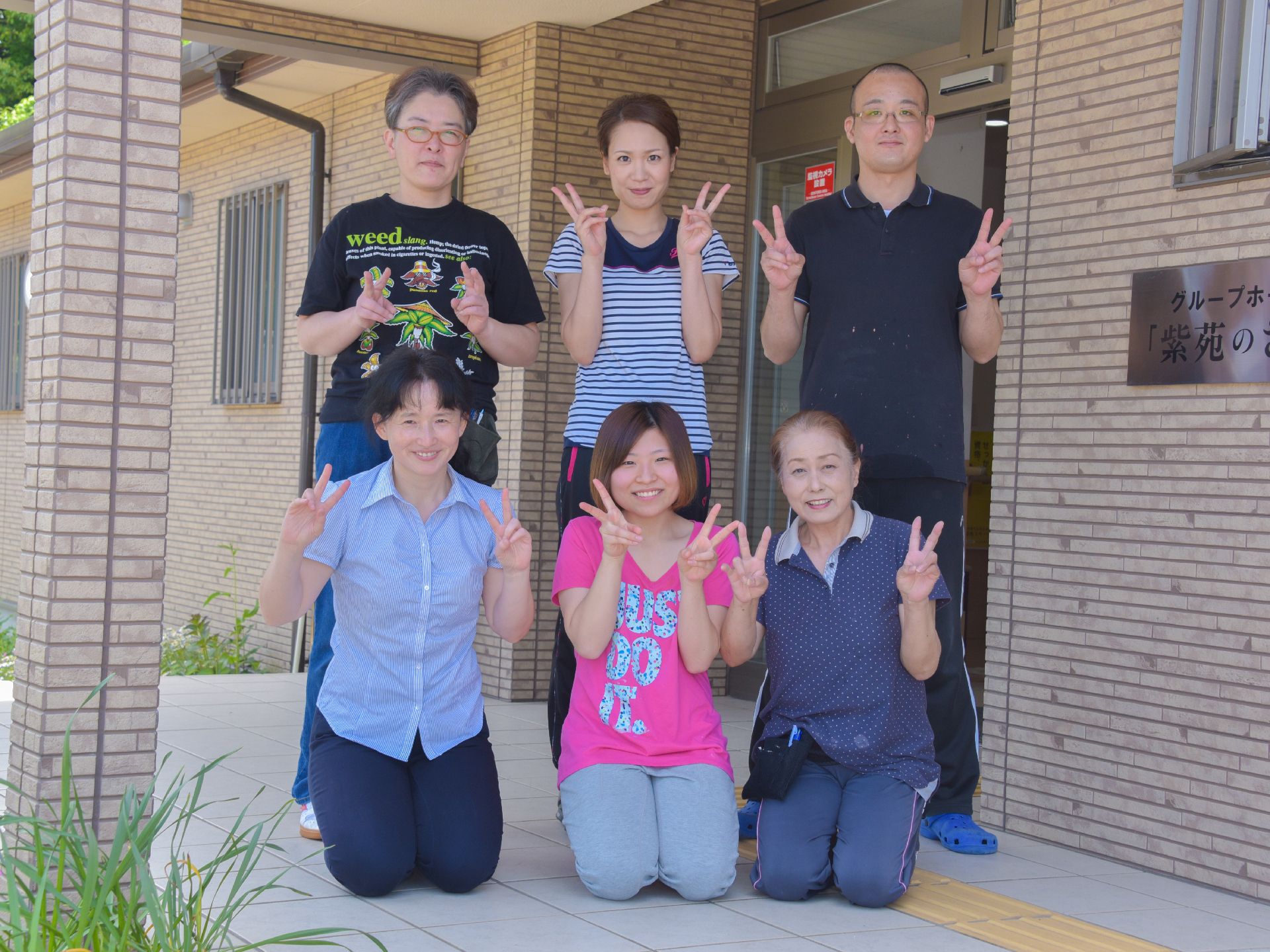 エントランスの外側でポーズを取って写真に納まる6人の施設スタッフ