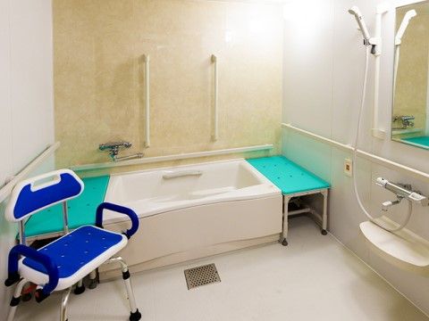 ユニットバスタイプの浴室の洗い場に、青と白のシャワー椅子が置いてある。浴槽の両側に、移乗台が設置されている。