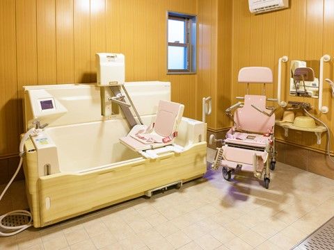 床がタイル張りされた浴室に、座位入浴が可能な介護浴槽が設置されている。洗い場にシャワー椅子が置いてあり、鏡と手すりが設置されている。