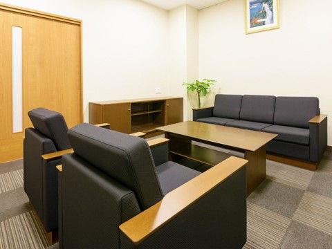 灰色の模様のタイルカーペットが敷かれた部屋に、黒いソファーとテーブルが置いてある。壁に絵画が飾られている。