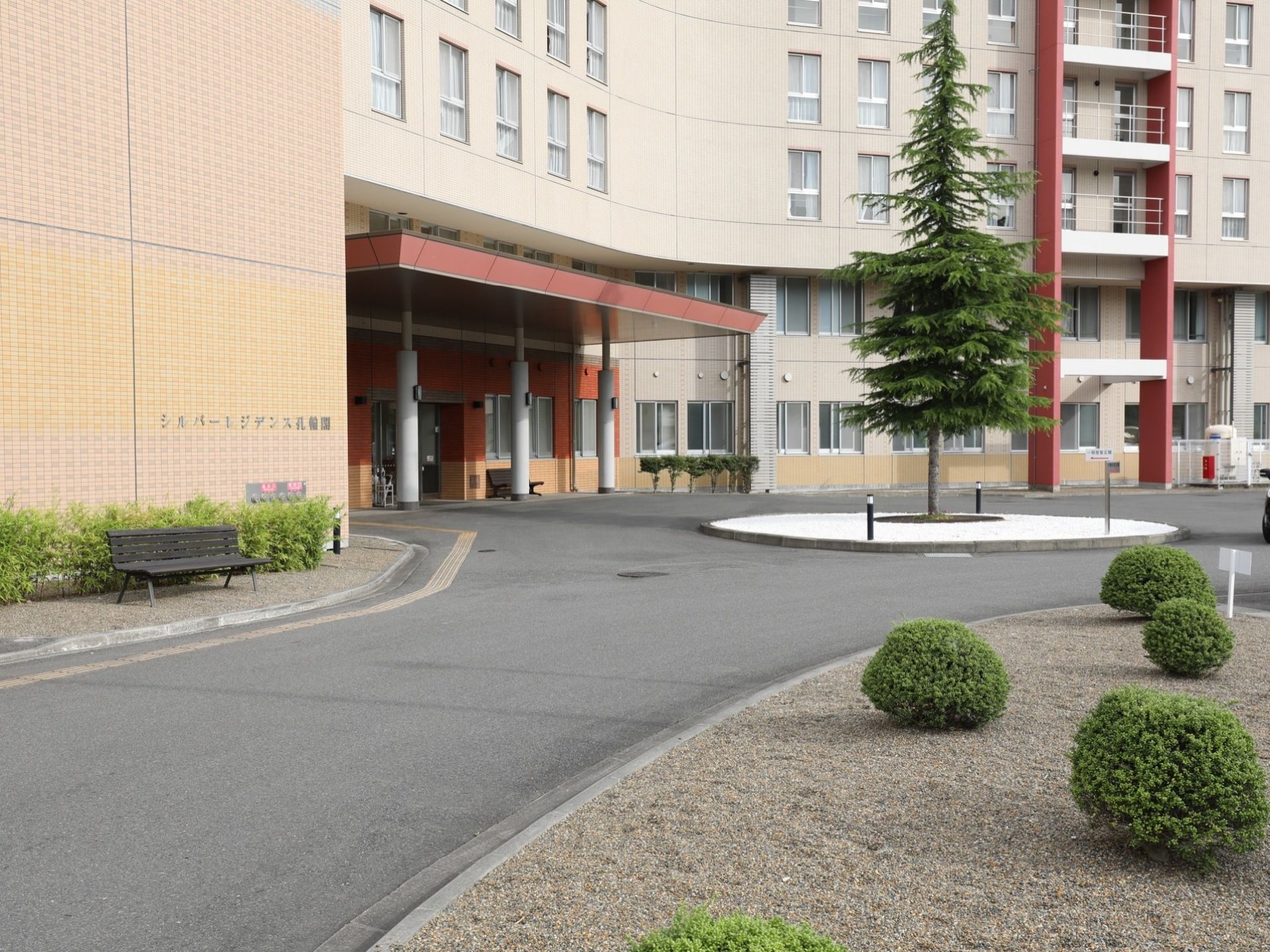 建物の正面入り口前には広いロータリーがある。玄関前に車を停めて送り迎えなどができる。植木があり、ベンチも置いてある。