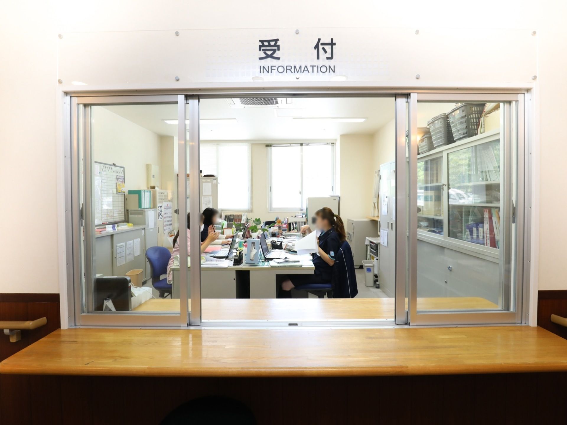 受付にはカウンターがあり、透明な窓からは中の事務室の様子を見ることができる。事務室ではスタッフの方が働いている。