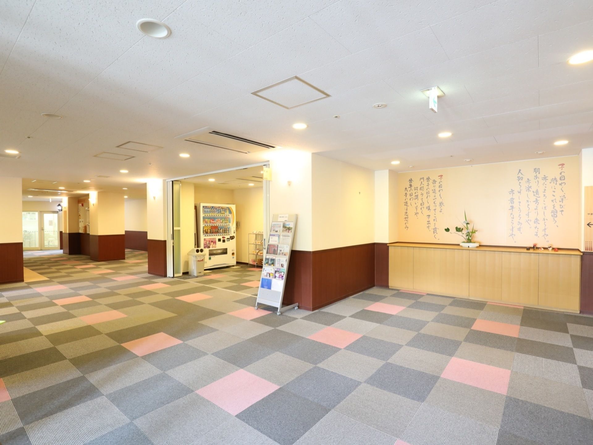 ロビーはじゅうたん敷きのスペースが広く、壁際の棚には生け花が飾ってある。壁には筆文字で論語が書かれている。