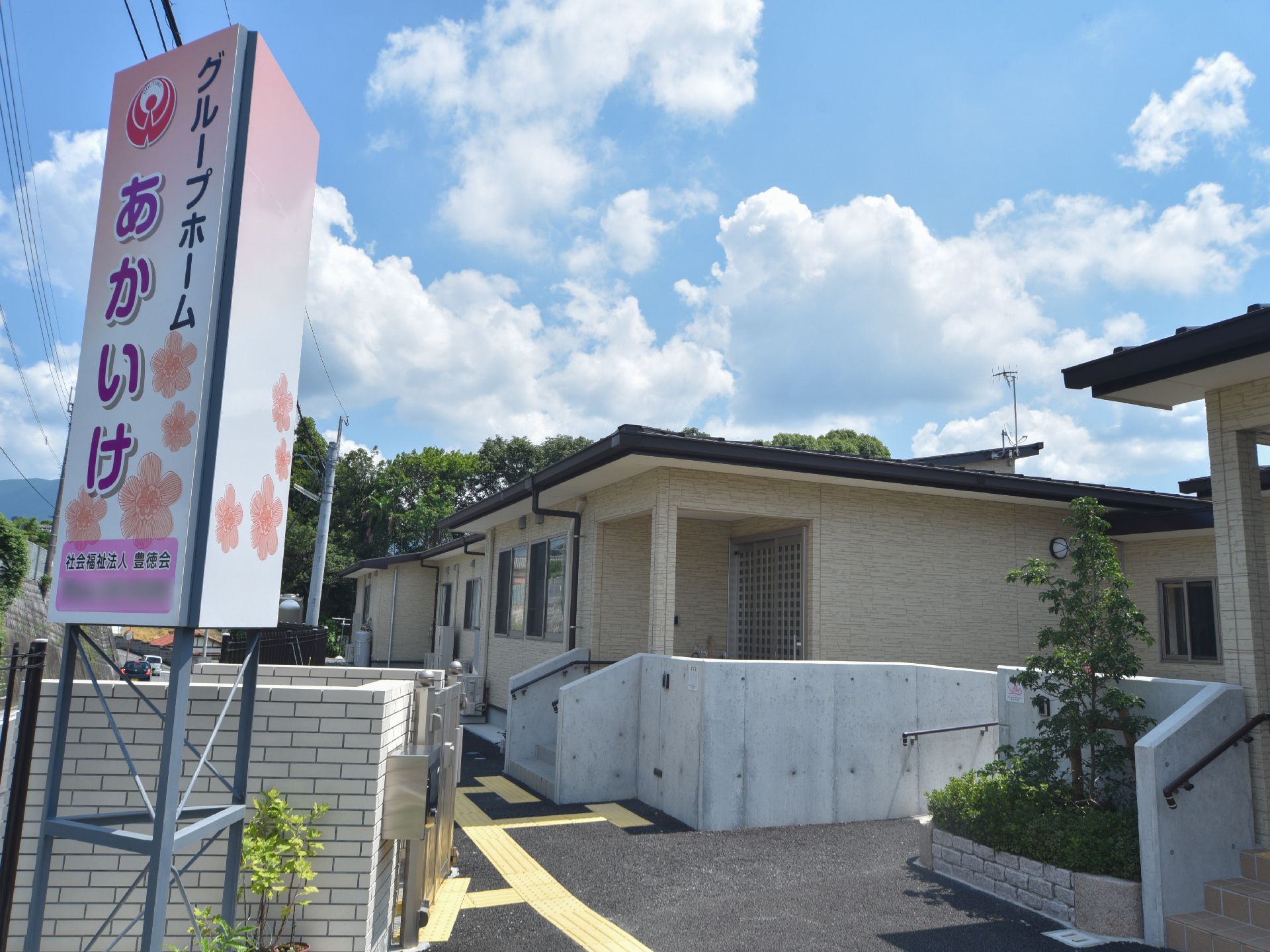 施設の入り口には、手すりがついた階段が設けてあり、掴まりながら玄関まで行くことができる。施設名が入った大きな看板が道路そばにある。