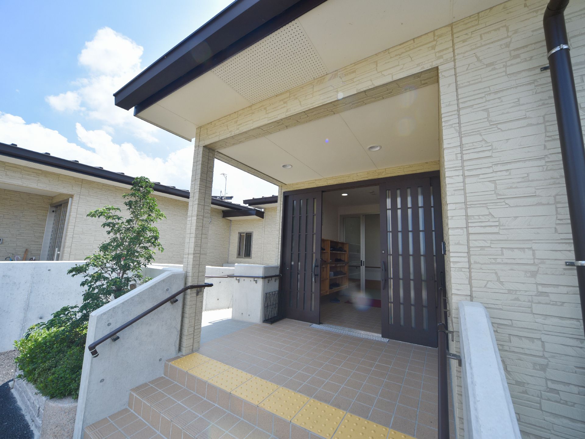 手すりと階段を上った先に、玄関がある。玄関の内部には、木製の靴箱がある。赤いマットがしいてあり、靴を履き替えて入館できる。