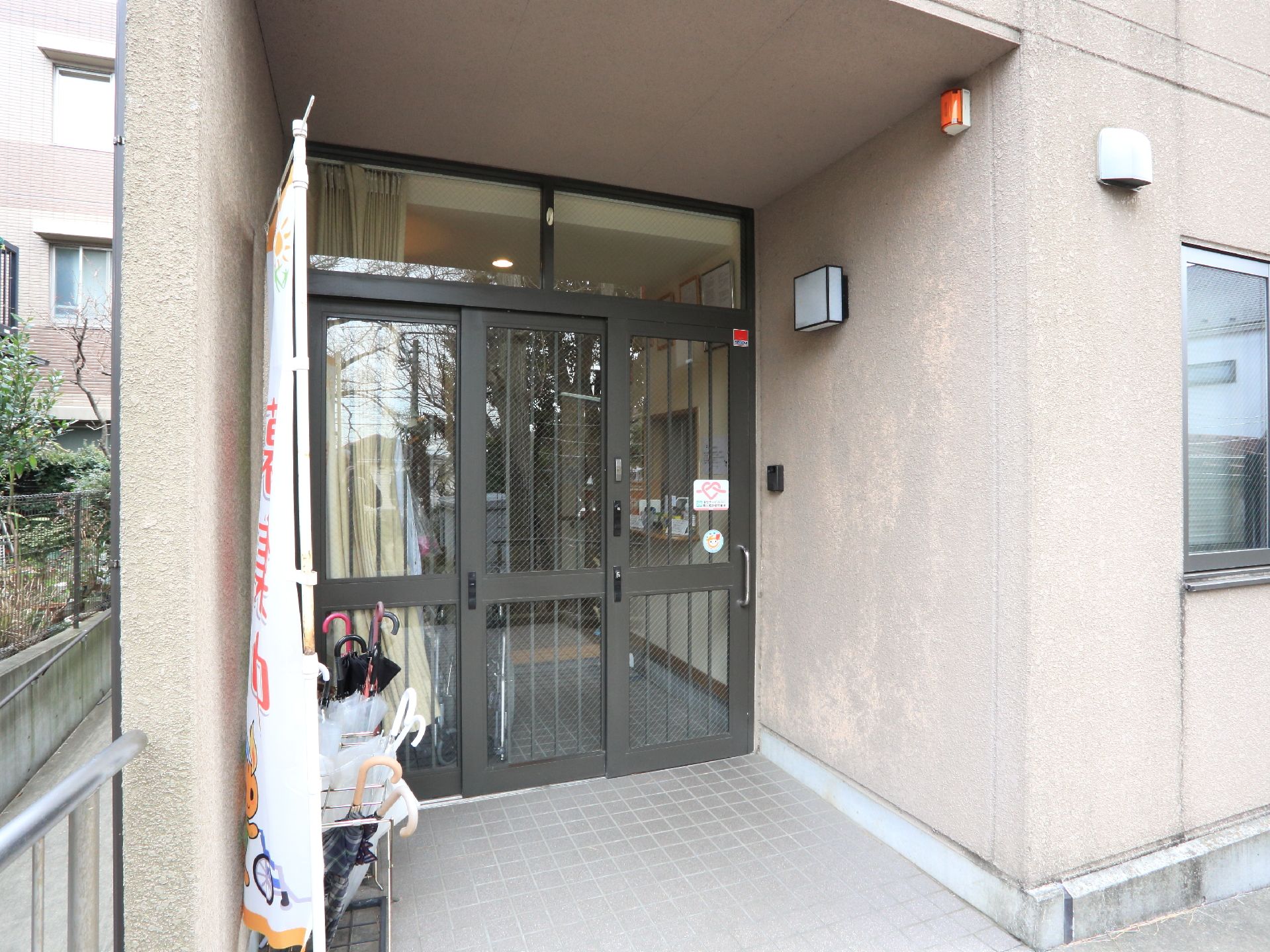 スライド式のドアが設置されている。タイル張りの床は段差がない。傘立てが準備されていて、たくさんの傘が置いてある。