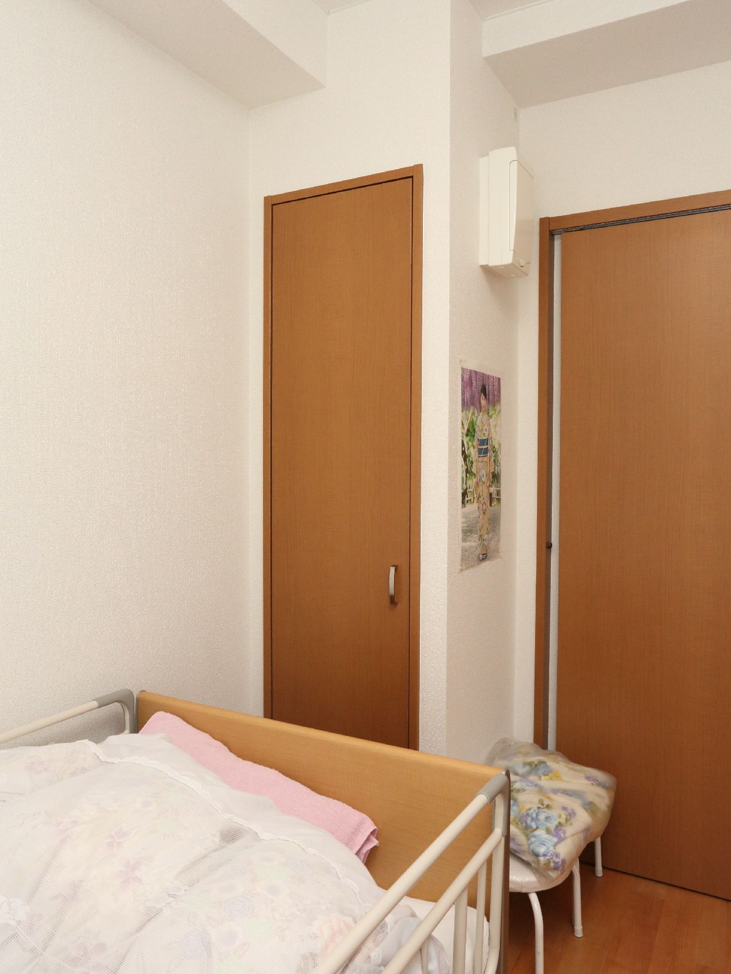 出入口付近には介護用ベッドが設置。物入れや補助いすもベッドのそばにあり便利。白い寝具は清潔感がある。