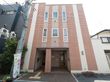 ３階建て施設の外壁は、やさしい色のコントラストが印象的である。入口前まで点字ブロックが設置されているのが見える。