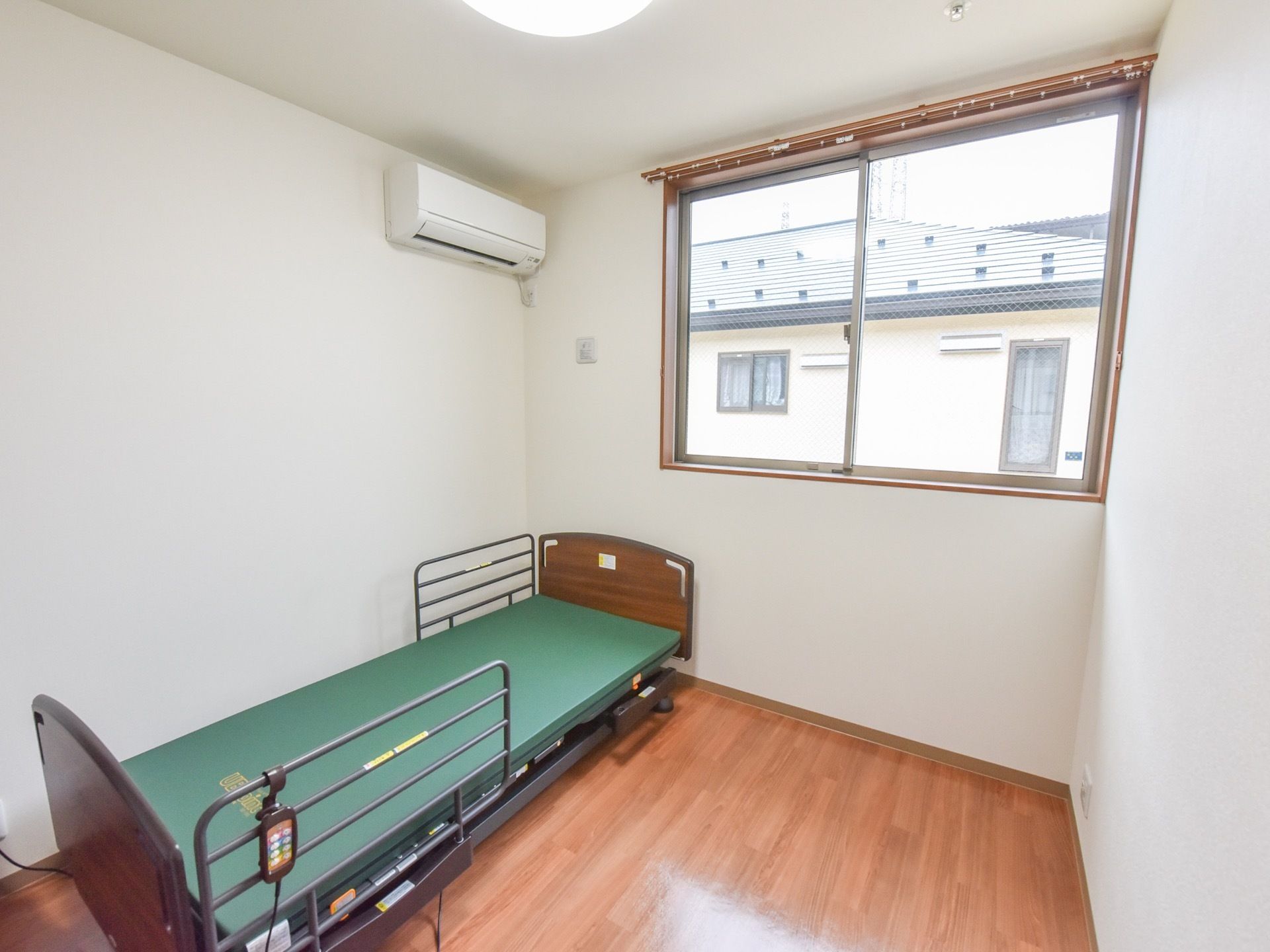 大きいベッドとエアコンが設置してある、個人で住める居室。床は木目調で、窓が大きく明るい雰囲気が感じられる。