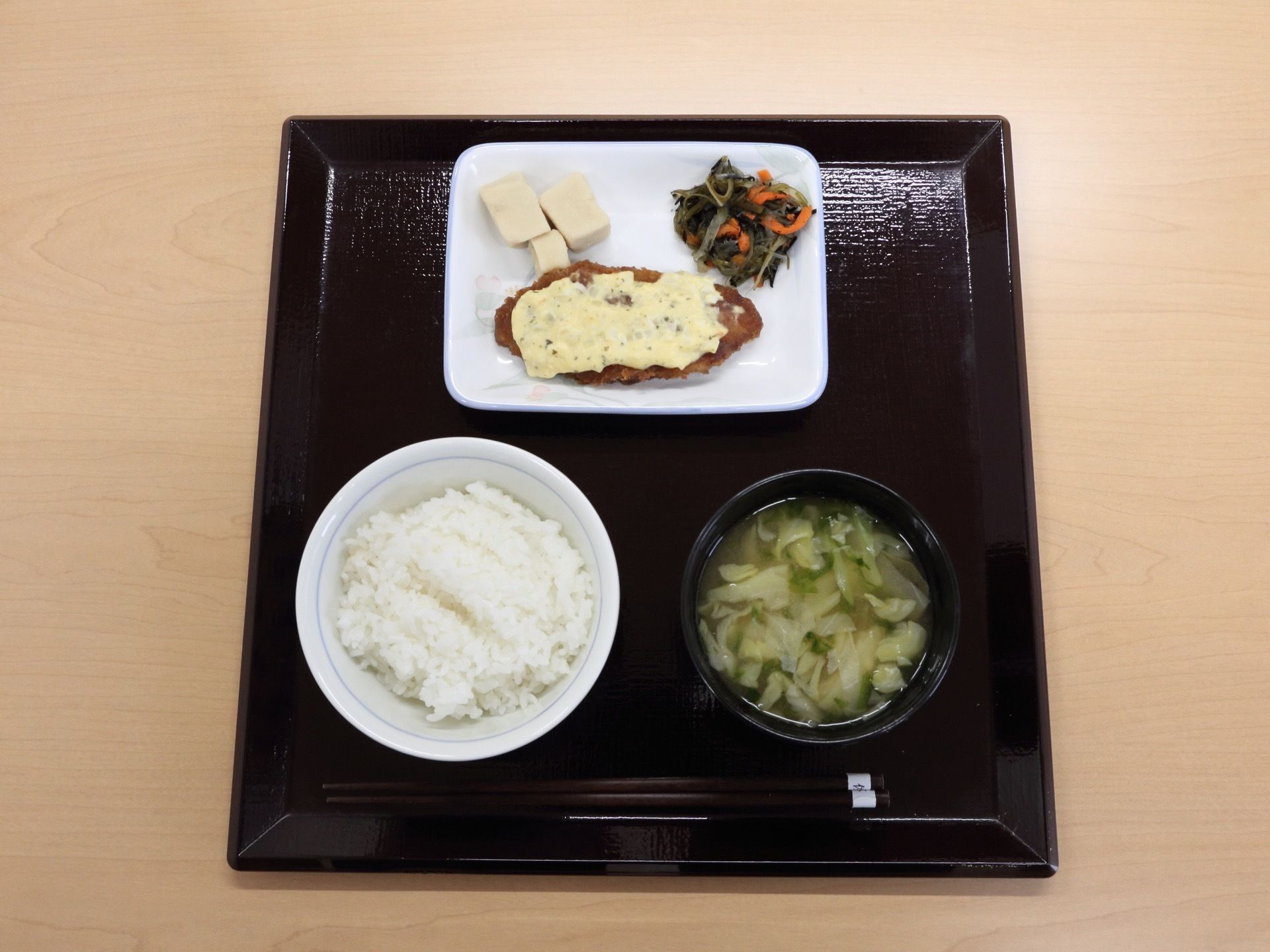 ある日の給食である。白ご飯、みそ汁、魚のフライタルタルソース掛け、高野豆腐、野菜の和え物である。栄養バランスが整っている。