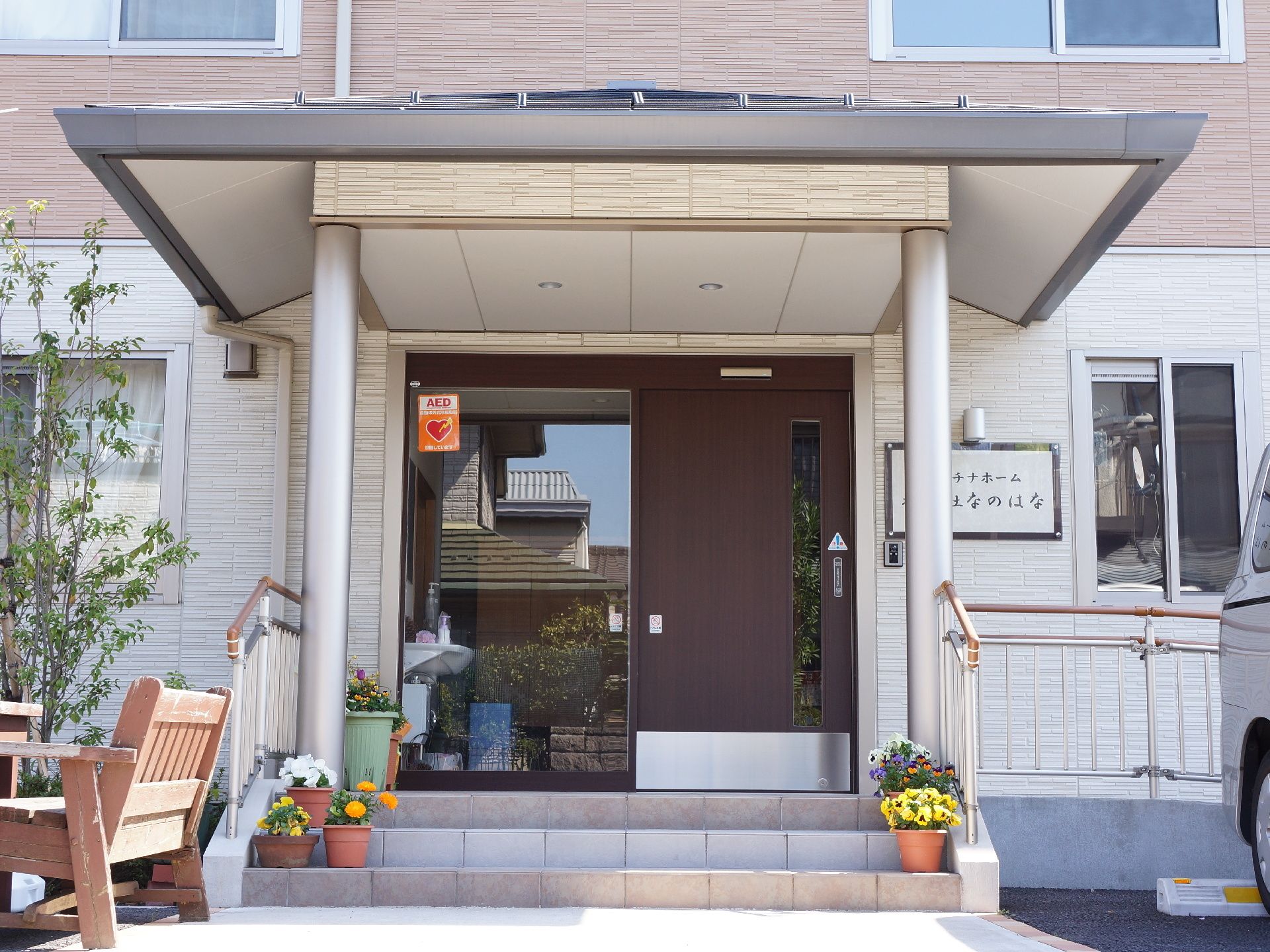 施設の入り口前には3段のステップがある。左右には手すりが設置されており、その下には花の鉢が複数置かれている。