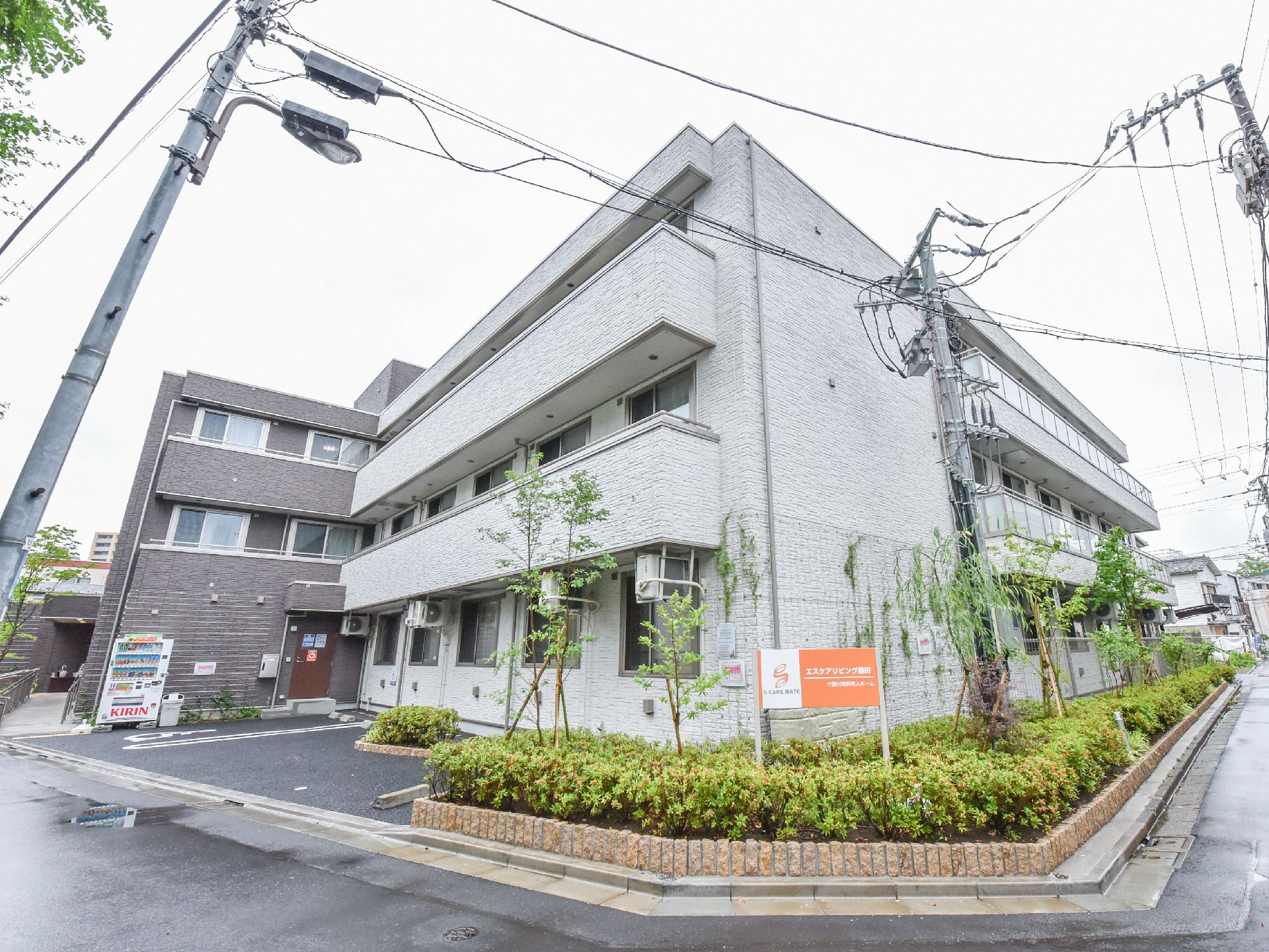 施設はブラウンとグレー系の部分に分かれている3階建ての建物である。外周には植え込みがあり、駐車スペースが設けられている。