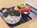 1人分の食事が黒いトレーにセットされている。うどんをメインにつけつゆとかき揚げなど、5つの器が並べられている。