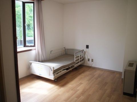 居室は広くフローリングの床で、明り取りの大きな出窓がある。また、両サイドに転落防止のガードがついた介護用ベッドが置いてある。