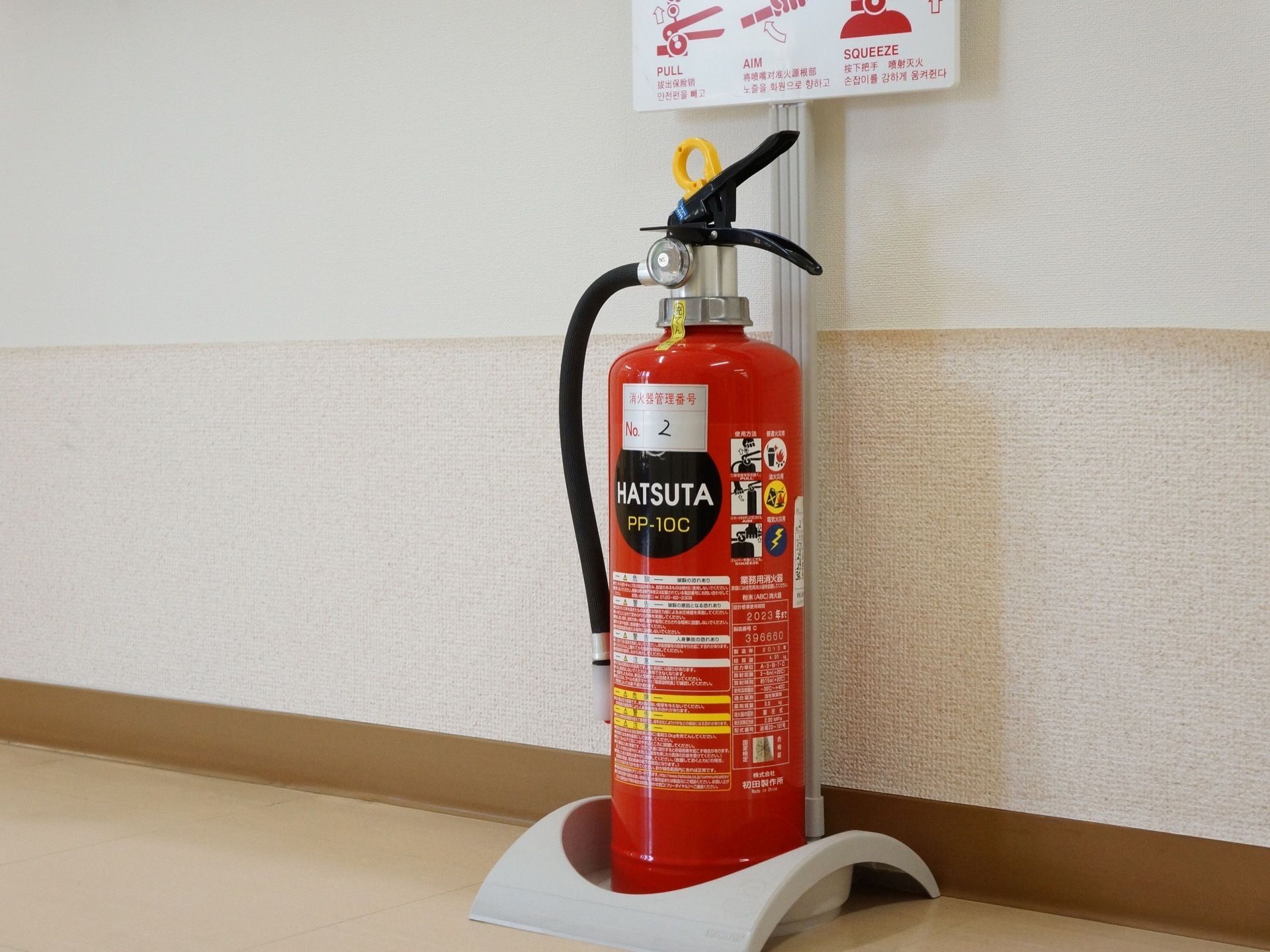 使い方の説明看板付きの未使用の消火器が、通路に置かれている。床はアイボリー色、壁は白色の配色である。
