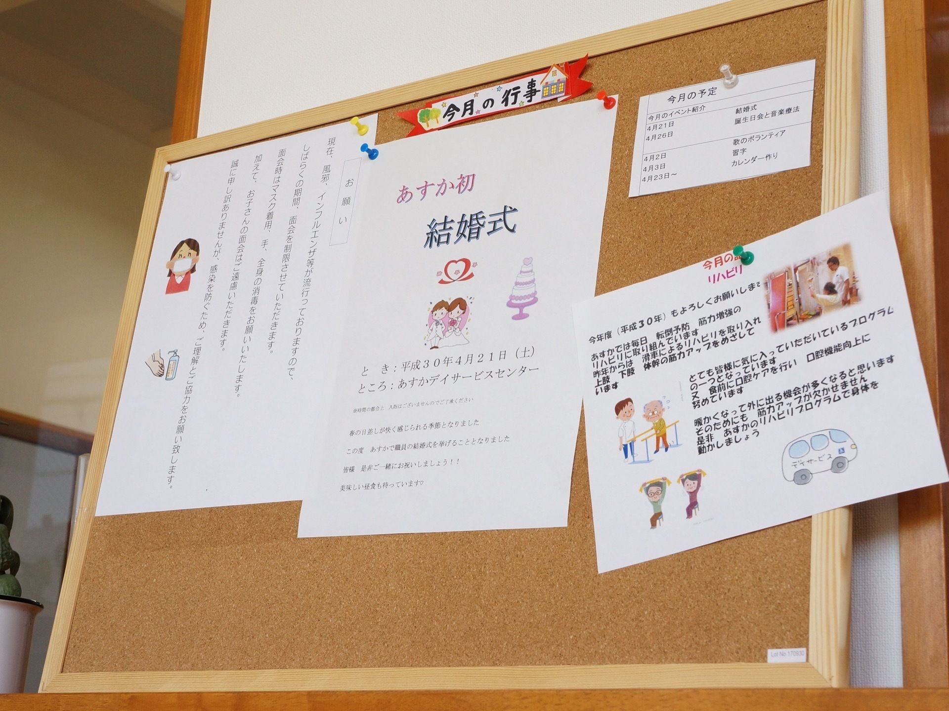 今月の行事予定などの掲示物がコルクボードにプッシュピンで貼られている。隣には多肉植物が飾られている。