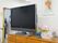 チェストの上にテレビ、花の飾り、虫よけ器具が置かれている。壁には絵が飾られている。消火器が置かれている。