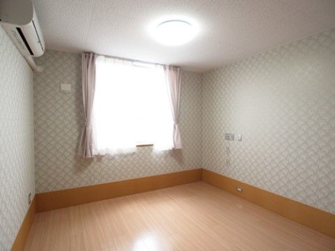 壁にエアコンが設置され、天井にシーリングライトが点灯している。腰高窓にカーテンとレースカーテンが掛けられている。