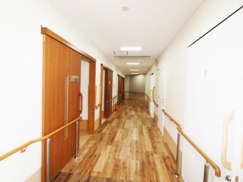 白いクロスの壁と木目のフローリングの床の長い通路である。両側の壁に手すりが設置され、天井に照明が取り付けられている。