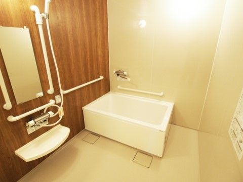 広々とした洗い場の壁に手すりとシャワーと鏡が設置されている。浴槽のそばの壁にも手すりと蛇口が取り付けられている。