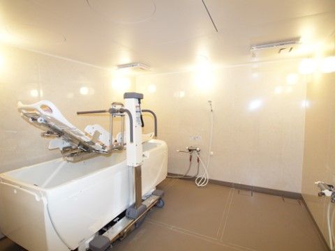 白く輝く浴室の壁に照明のライトが反射している。壁際に寝位入浴が可能な介護浴槽が置いてあり、リフトが取り付けられている。