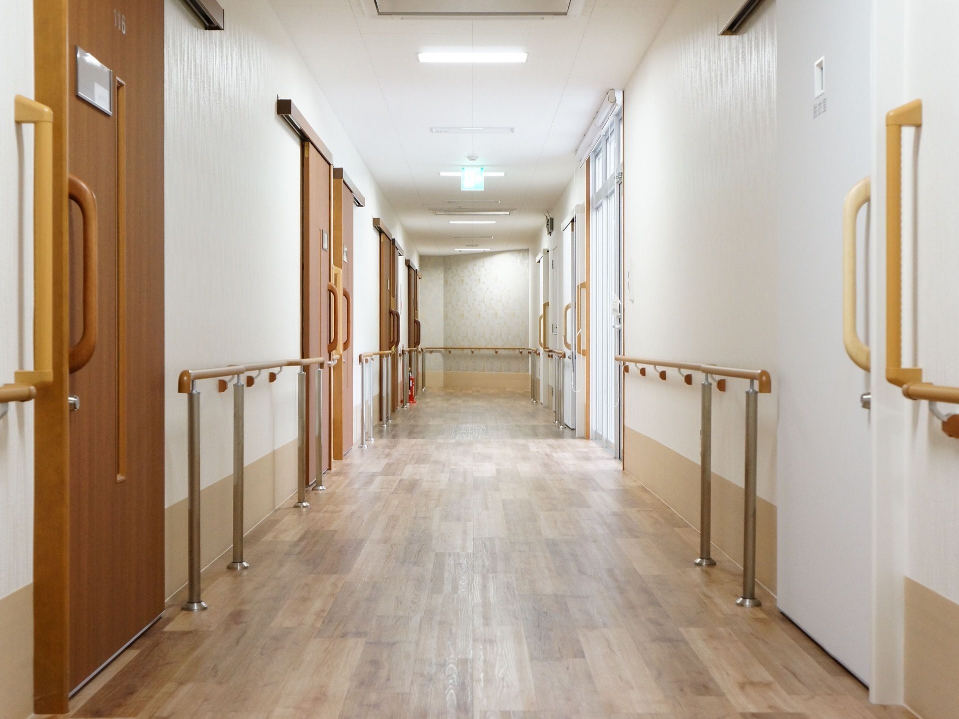 白い壁の明るい廊下になっている。手すりが壁全面に設置されており、安全に移動することができる。床は落ち着いた色のフローリングである。