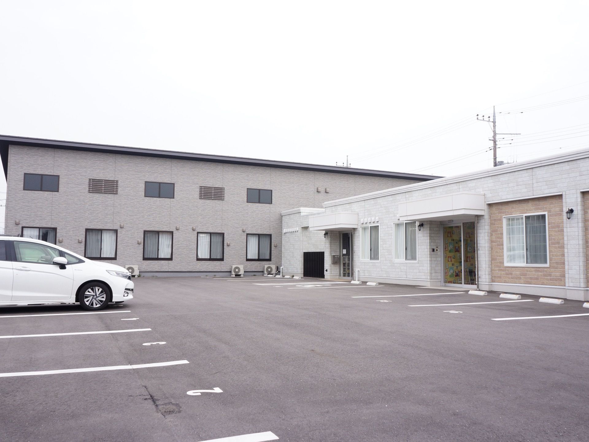 多くの車が駐車可能な広い駐車場と、白とベージュ色の平屋の建物