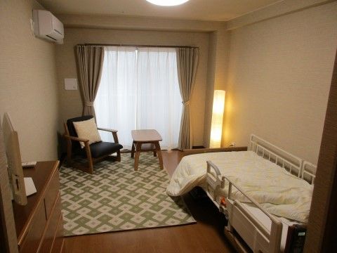 入居者様の居室。空調が完備された広々とした一室で、ブラウンのフローリングやホワイトの壁面で落ち着いた雰囲気となっている。