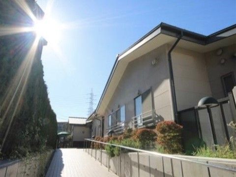 垣根と建物に挟まれた、幅の広いなだらかな斜面の手すりつきスロープ