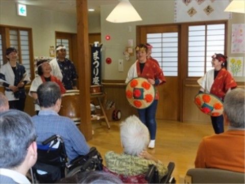 花笠と法被で出し物をする人達を、座って眺める入居者