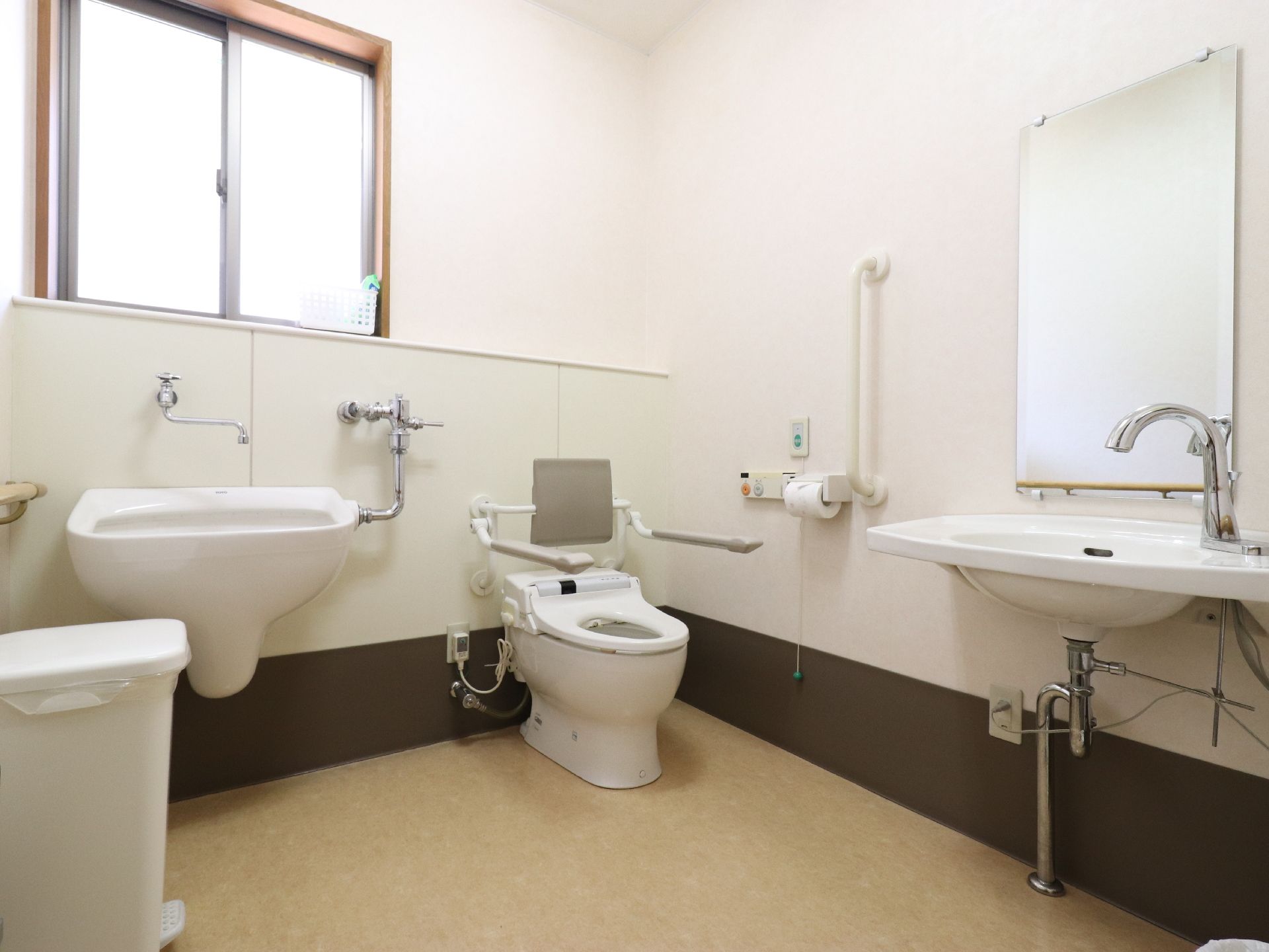 窓から採光が明るく清潔感がある。温水シャワー付のトイレには背もたれつきの肘掛けが付いている。壁には手すりとナースコールも設置されている。