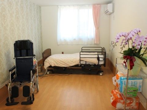 部屋の中に介護ベッドと車椅子が置かれ、右には胡蝶蘭が飾っているパイプ棚