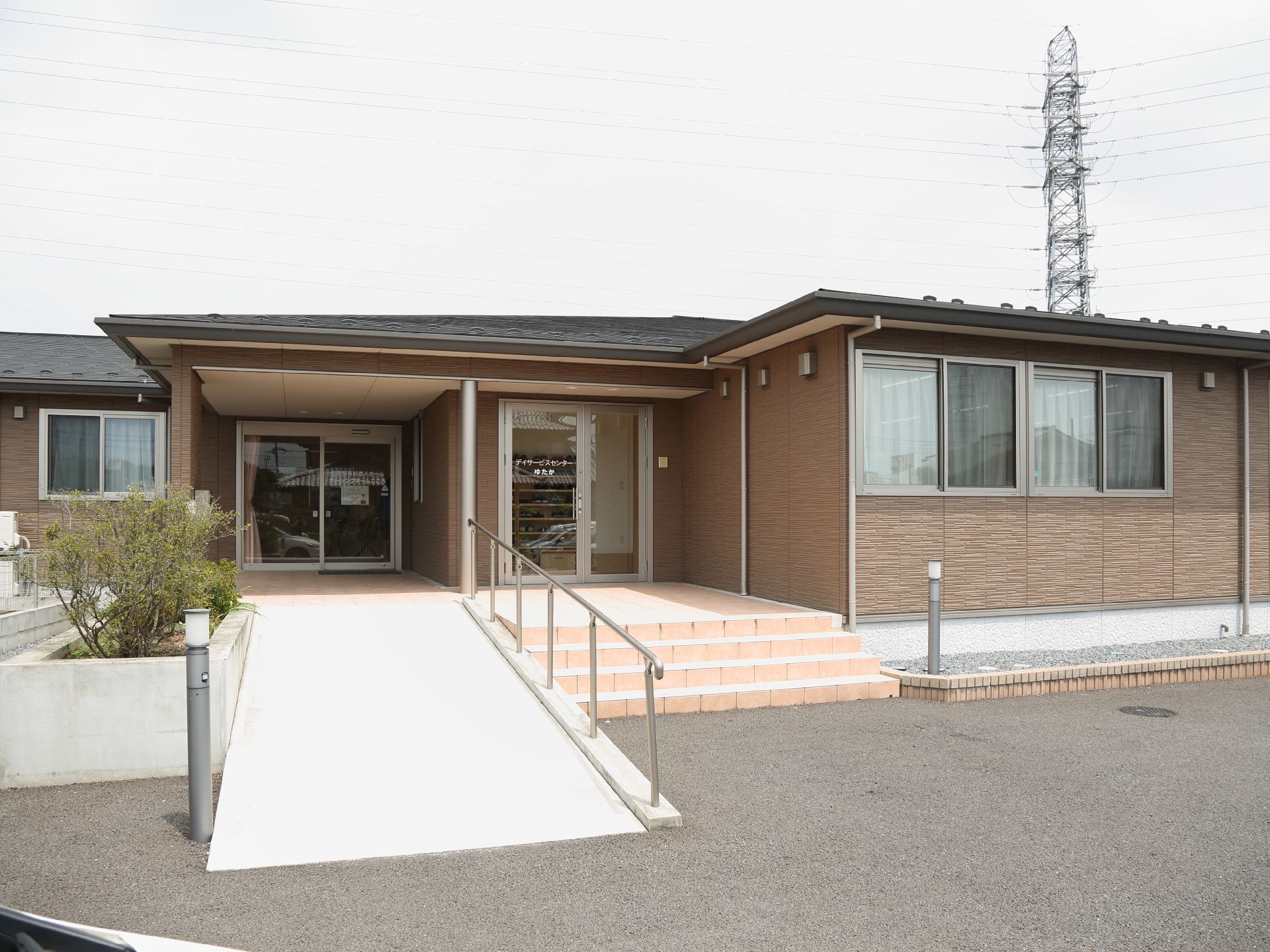 正面には平屋建ての建物が建っている。その手前の左側にはスロープがあり、右側には階段が付いている。外壁は茶色で、屋根は黒色になっている。