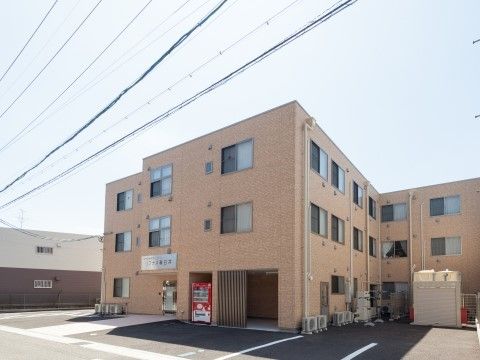 前は駐車場で、広い敷地の中に立つベージュの四角い3階館建物