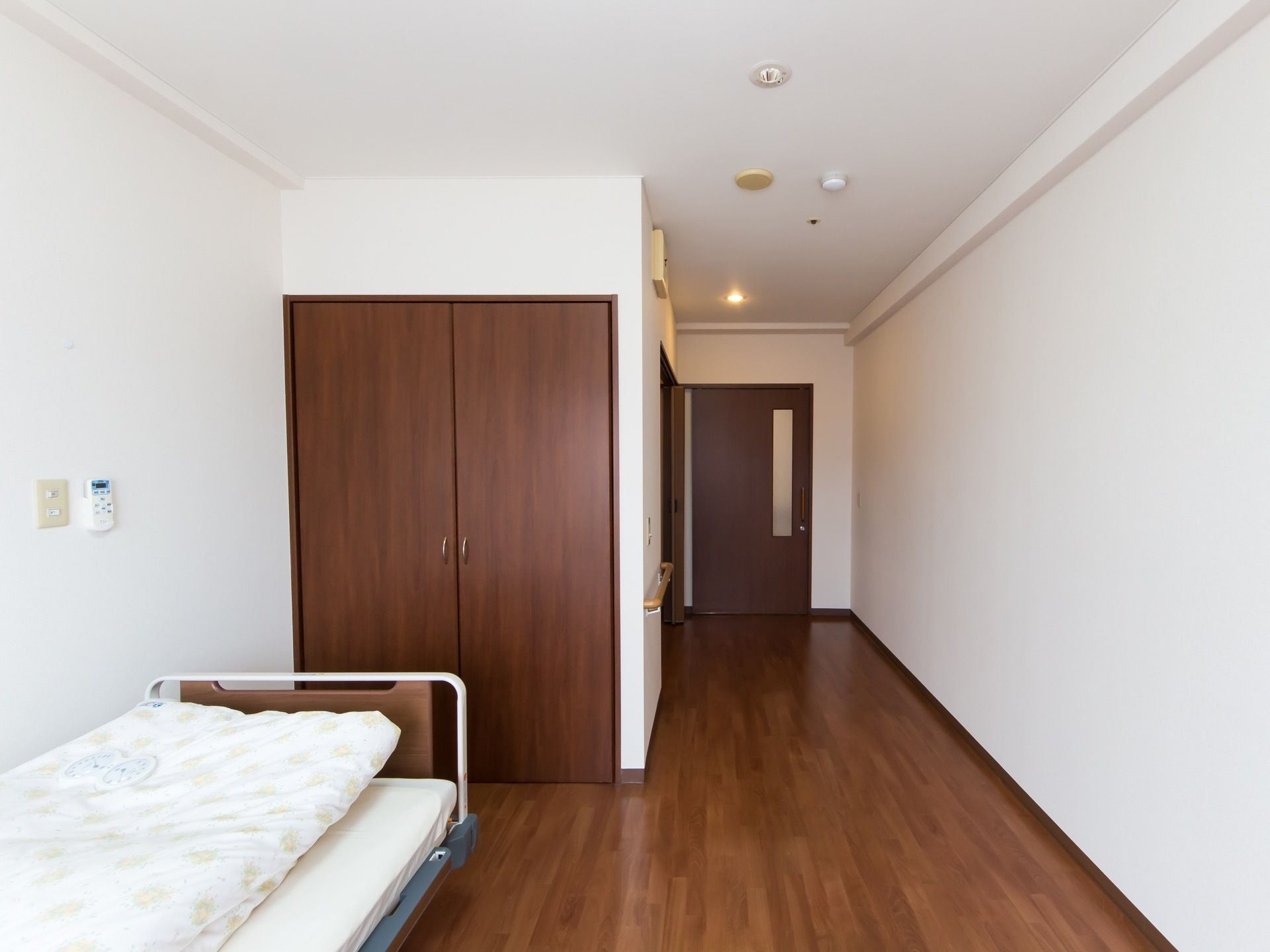 居室の壁は白色、床面や扉は濃い茶色になっている。入口付近の天井に埋め込み式のダウンライトが設置されている。