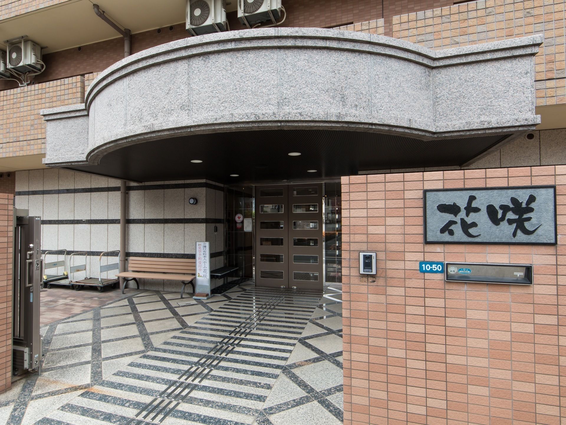 レンガ積み模様の門柱に、大きな文字で施設名称が書かれた表札が掲げられている。玄関の前には、アーチ状にせり出した大きなひさしがある。