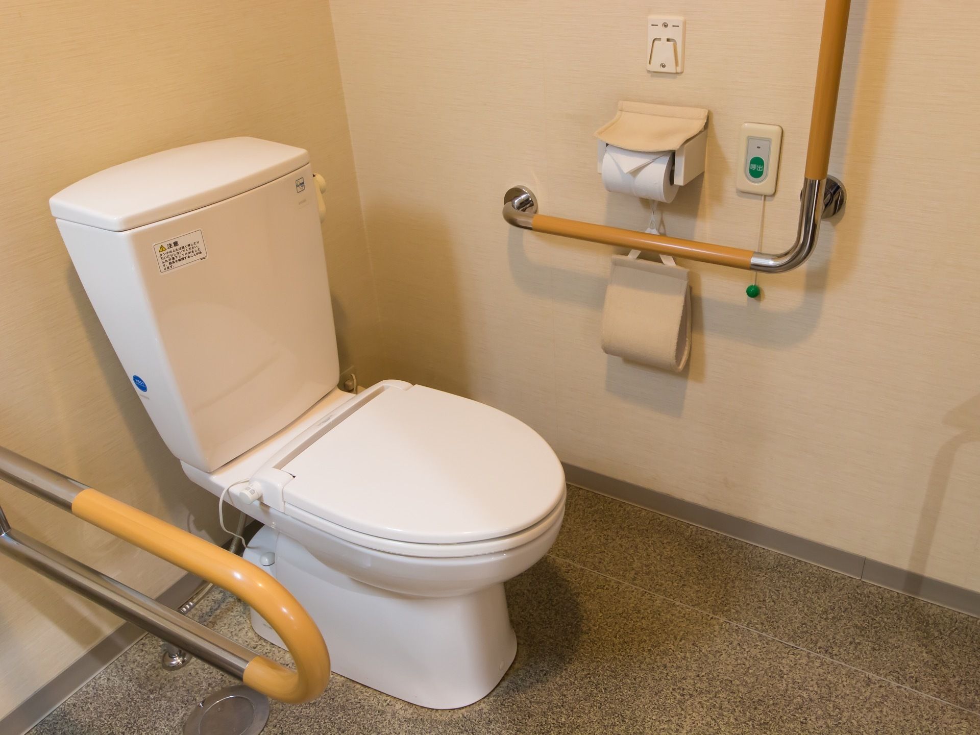 トイレの壁に、緊急呼び出しボタンが設置されている。先端には緑色の玉がついた紐がぶら下がっている。予備のペーパーを入れて置くホルダーがある。