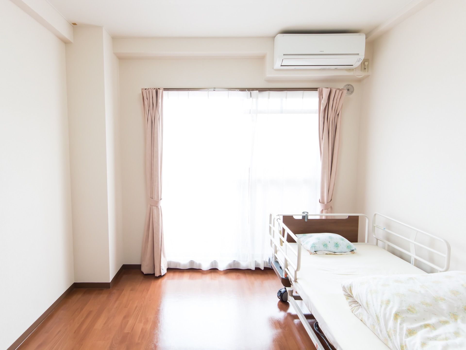 居室には掃き出し窓があり、その上の壁の天井近くにエアコンが設置されている。ベッドには転落防止柵がついている。