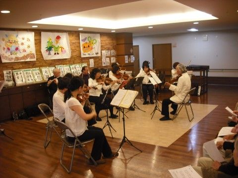 フローリングのホールで椅子に座ってバイオリンとフルートを演奏する楽団