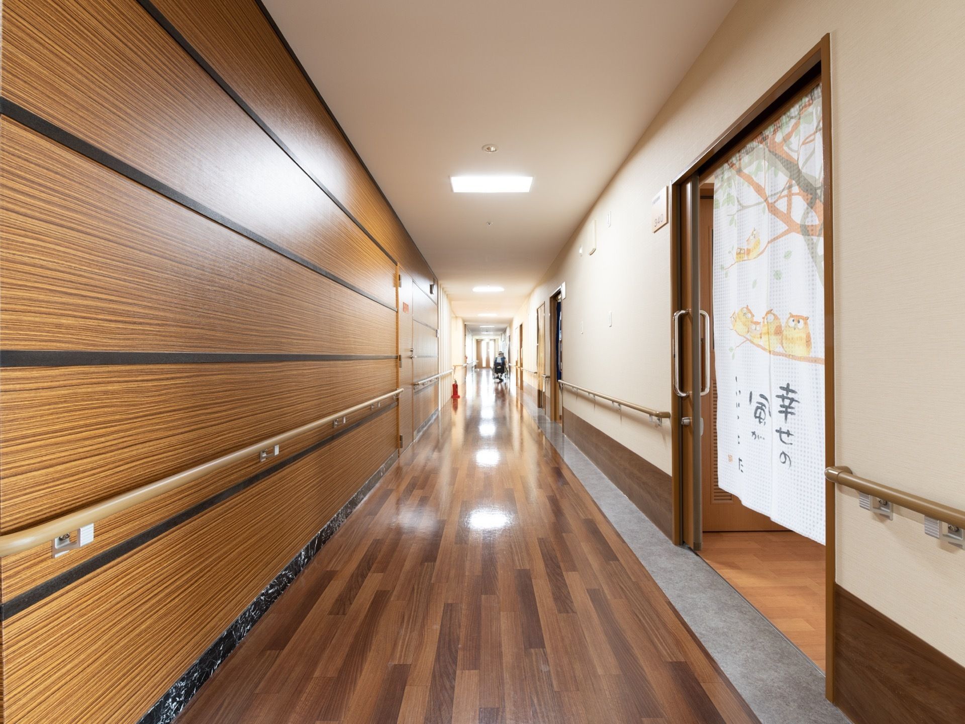 落ち着いた色合いの木目の廊下は、明るい白熱灯が照らし輝いている。各所には歩行補助のための手すりがあり、各部屋のドアはスライド式になっている。
